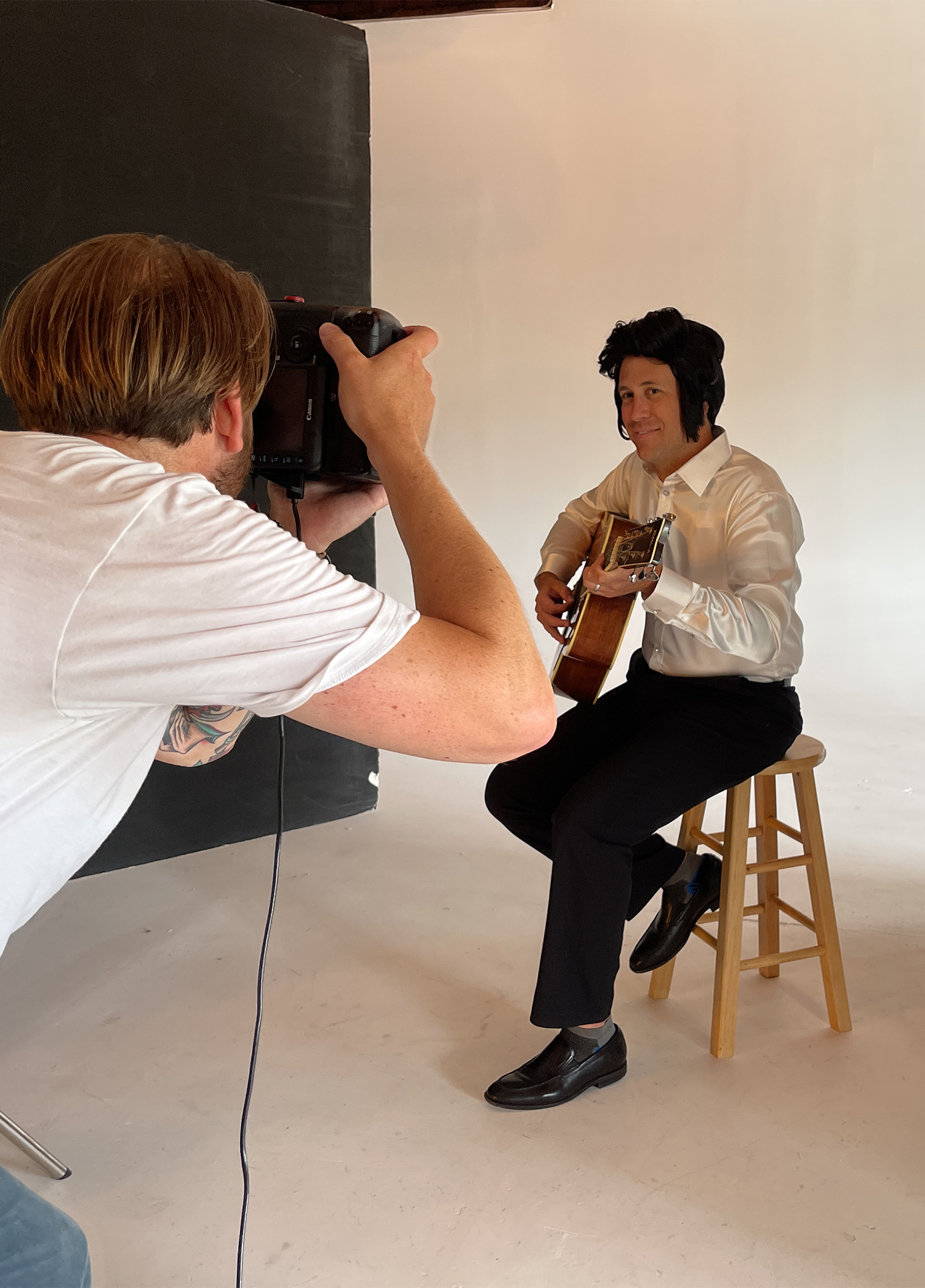 A man is taking a picture of a man playing an acoustic guitar.