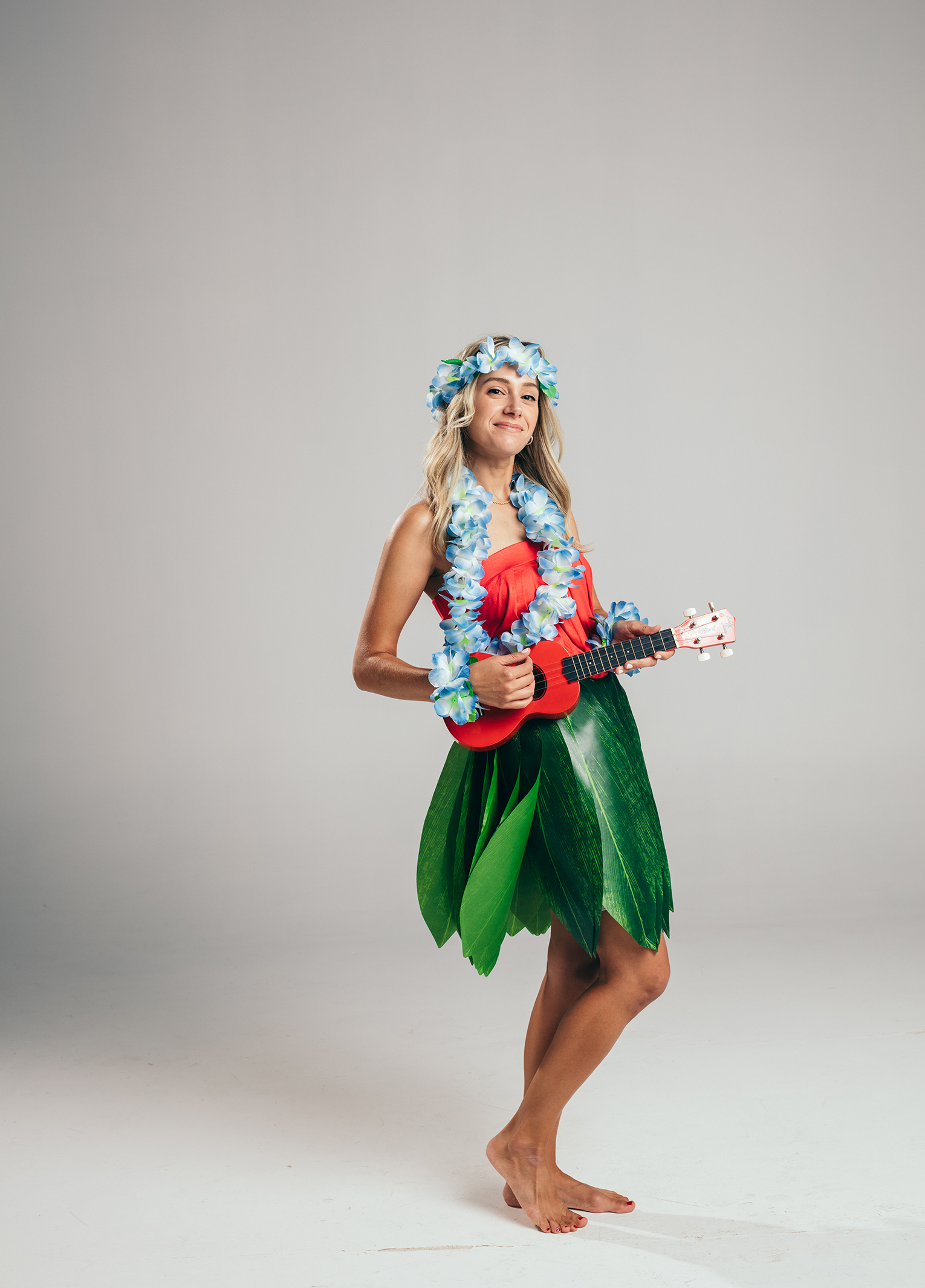 A woman in a hawaiian garment holding a ukulele.