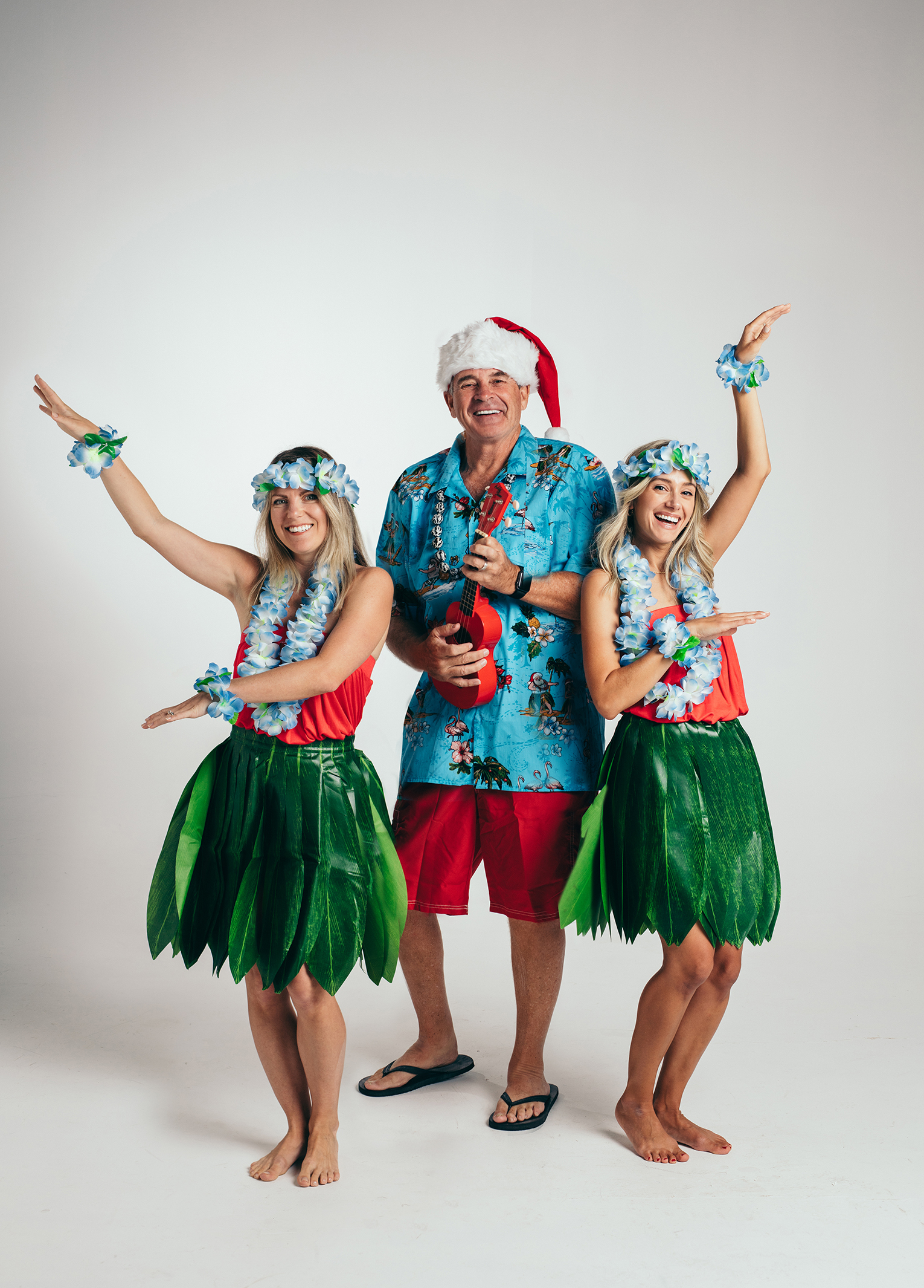 Three people dressed in hula skirts and santa hats.