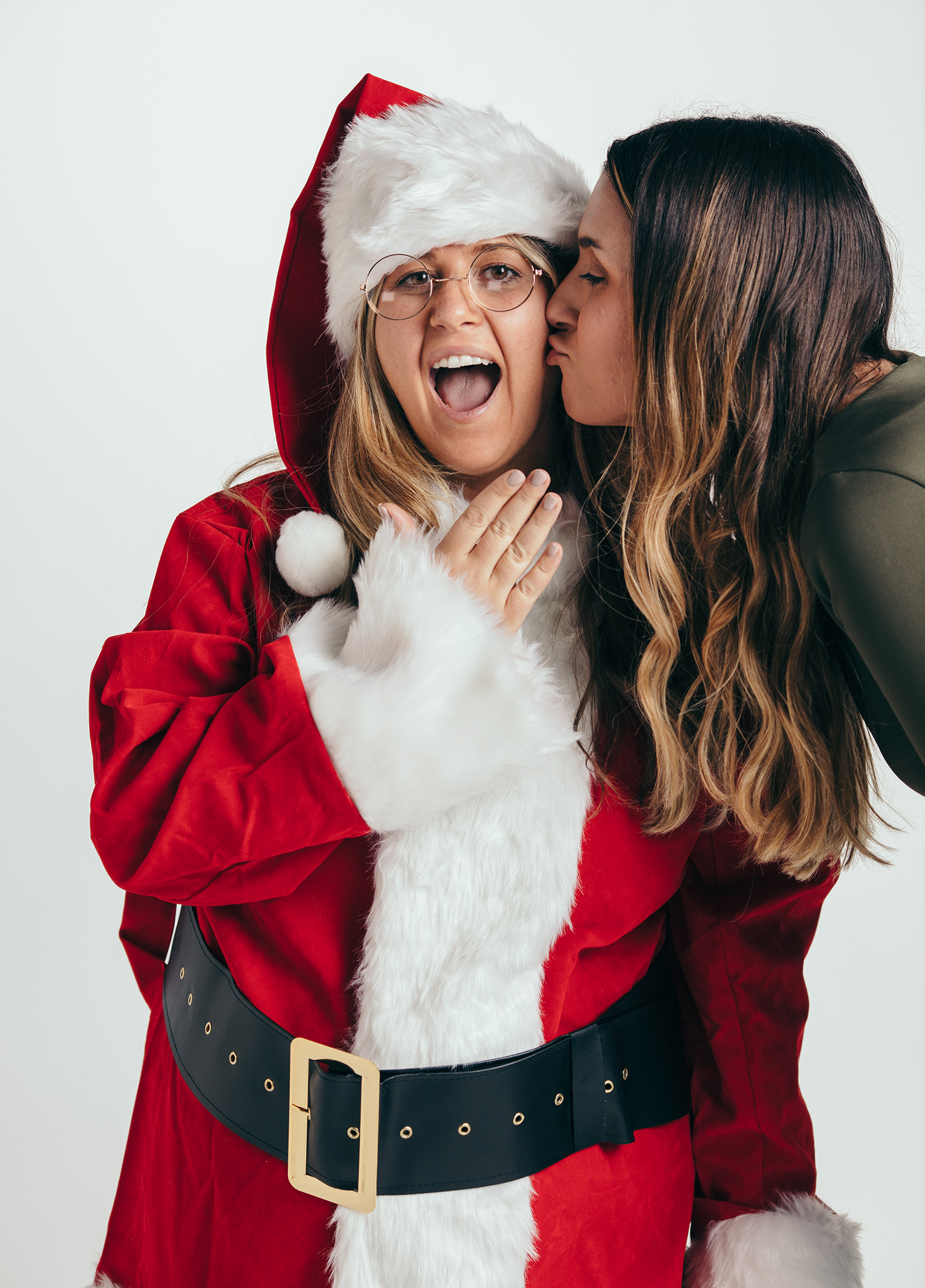 Two women in santa claus costumes kissing each other.