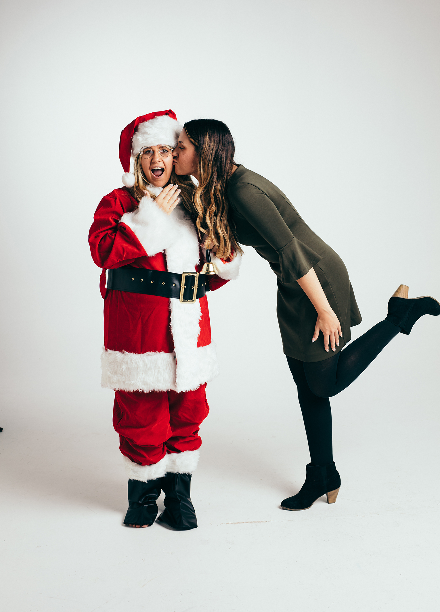 A woman kisses a santa claus in a studio.