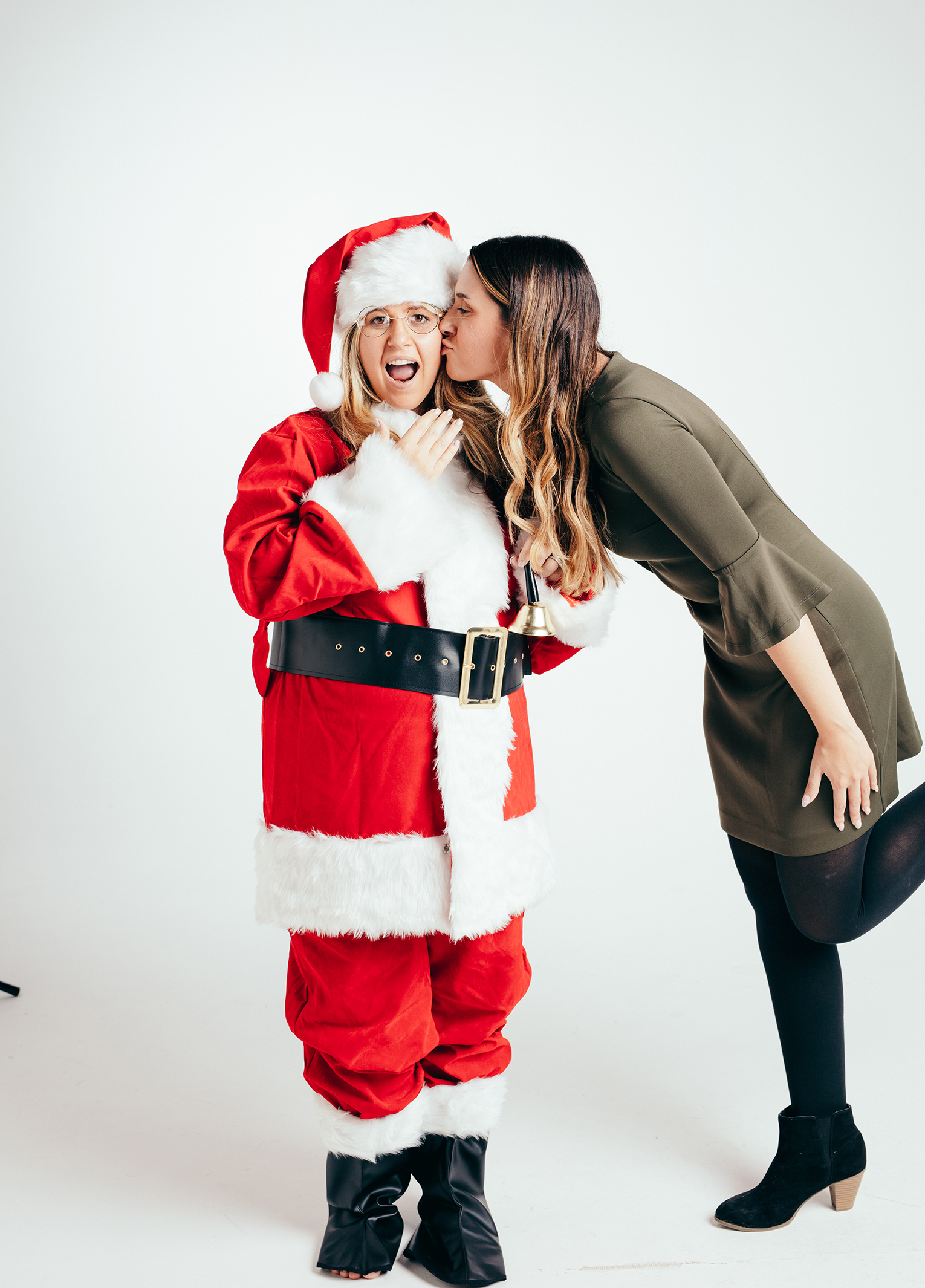 A woman kisses a santa claus in a studio.