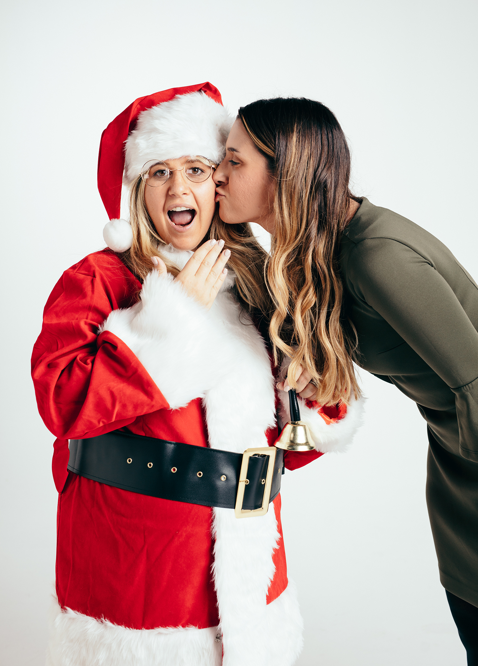 A woman kisses a santa claus in front of a white background.