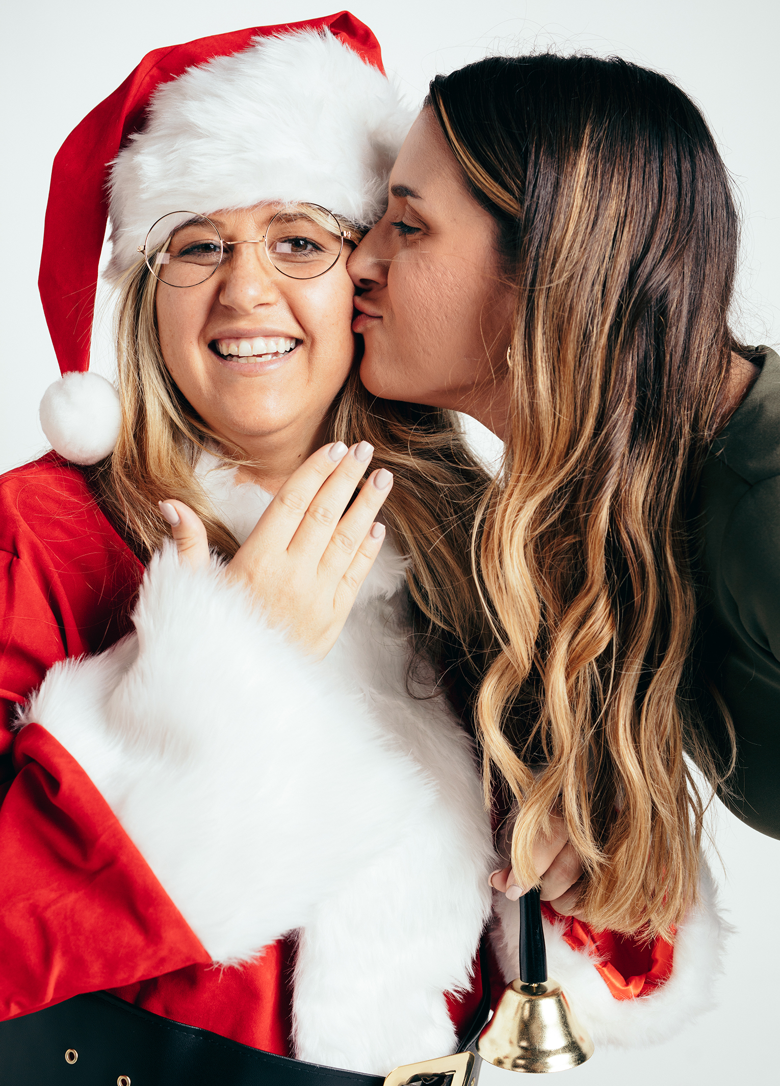 Two women in santa claus outfits kissing each other.