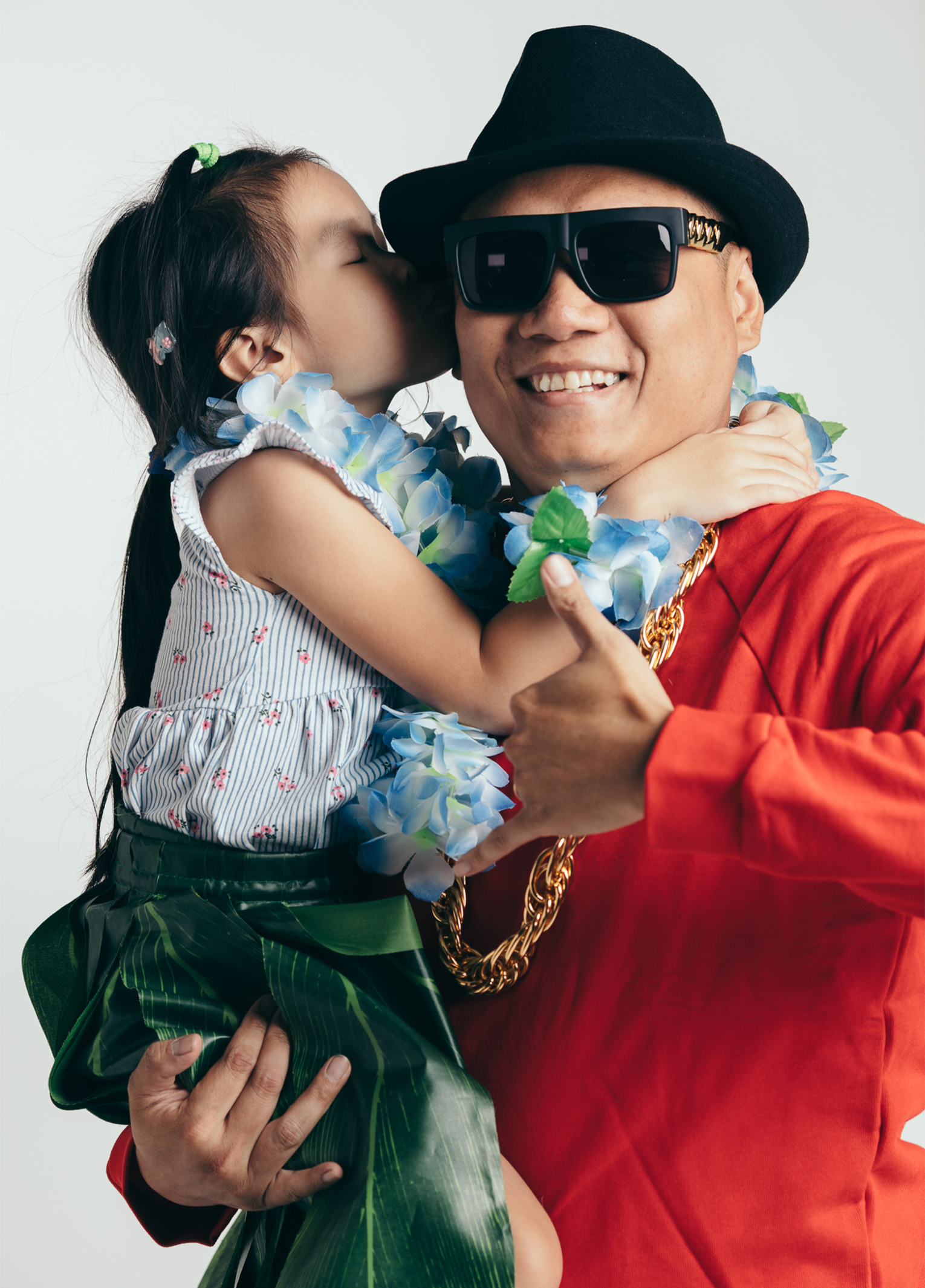 A man in a red shirt and sunglasses kissing a little girl.