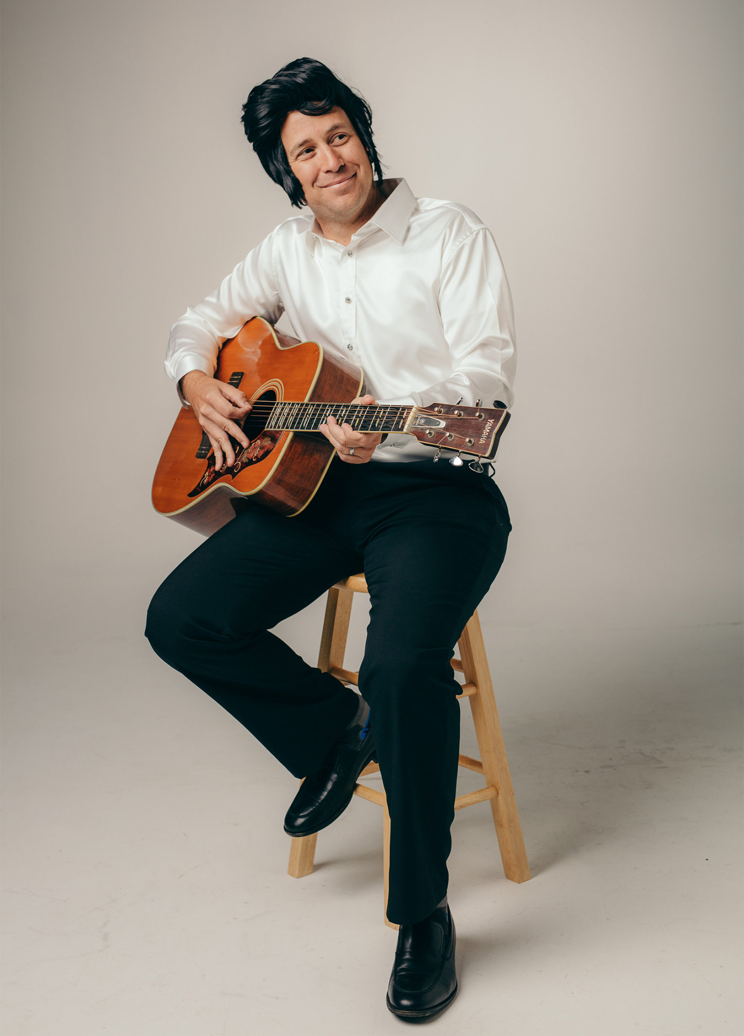 A man sitting on a stool holding an acoustic guitar.