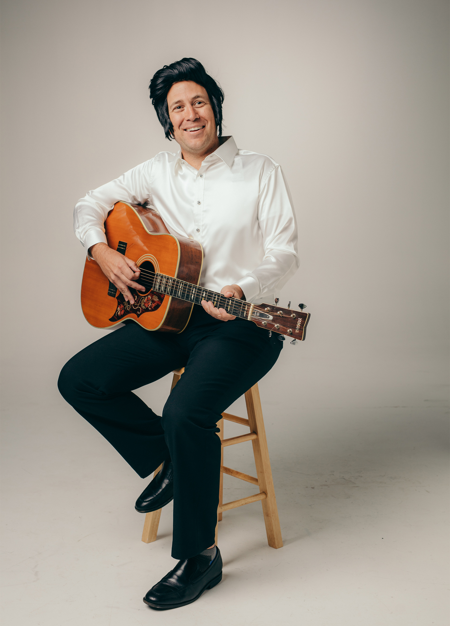 A man sitting on a stool with an acoustic guitar.