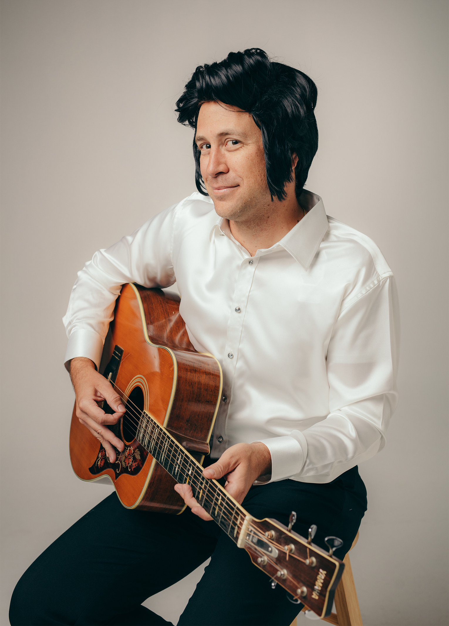 A man sitting on a stool holding an acoustic guitar.