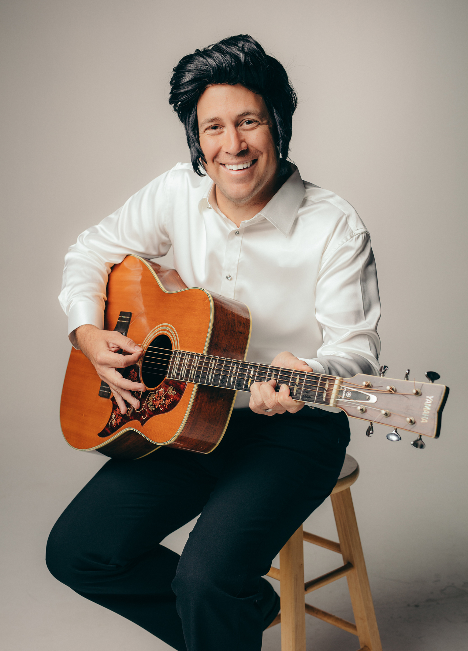 A man sitting on a stool holding an acoustic guitar.