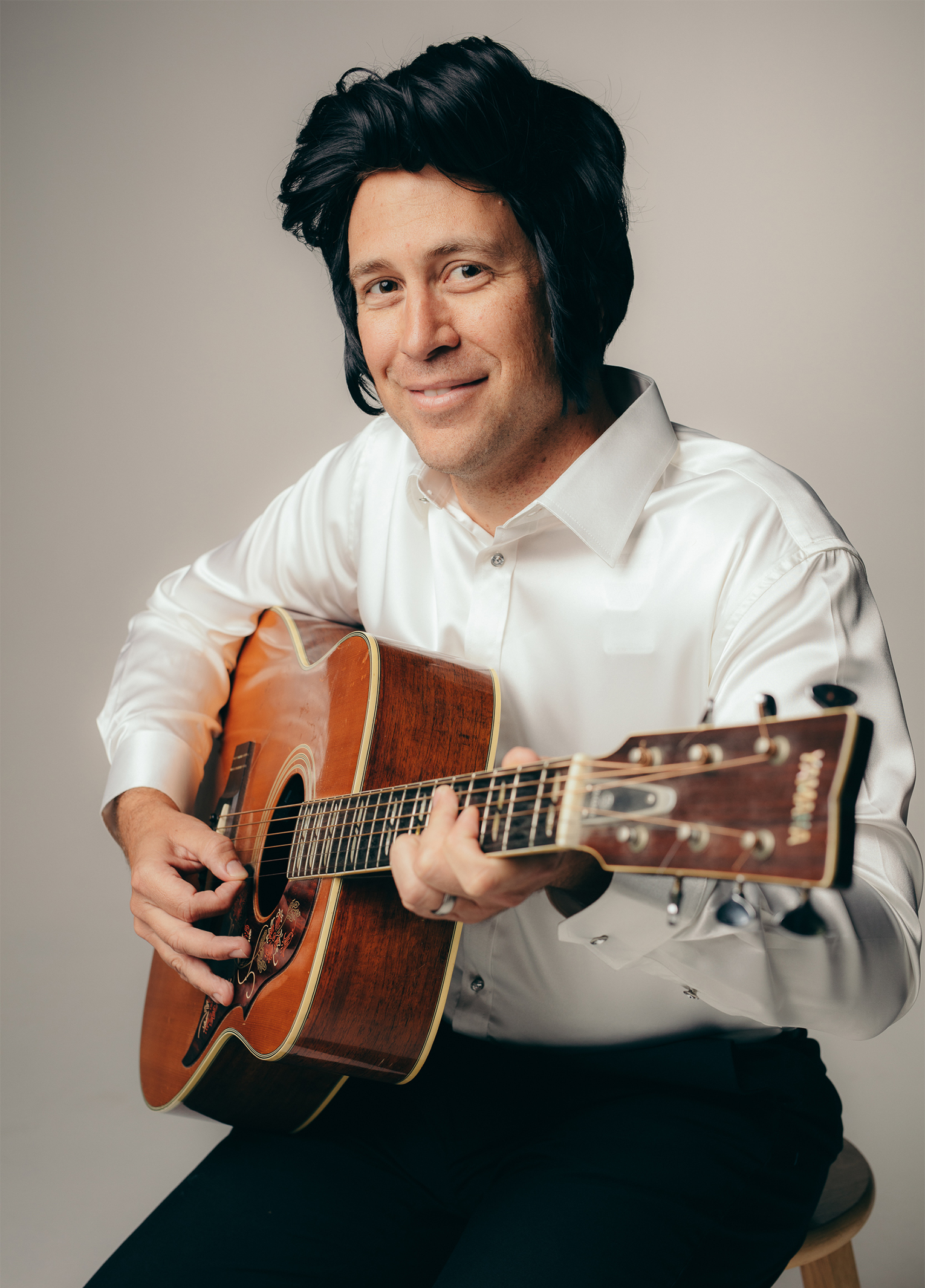 A man sitting on a stool holding an acoustic guitar.