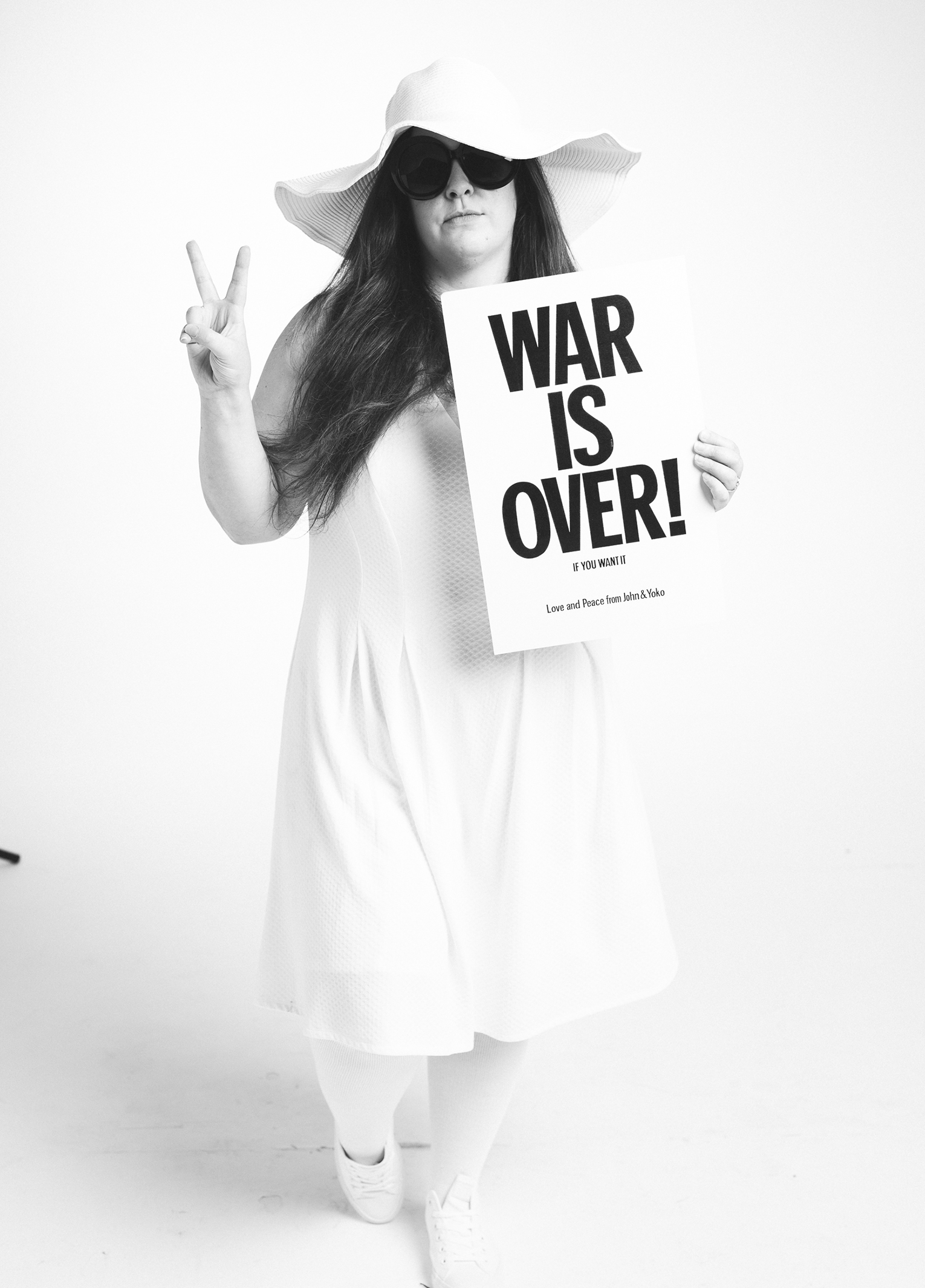 A woman in a white dress holding a sign that says war is over.