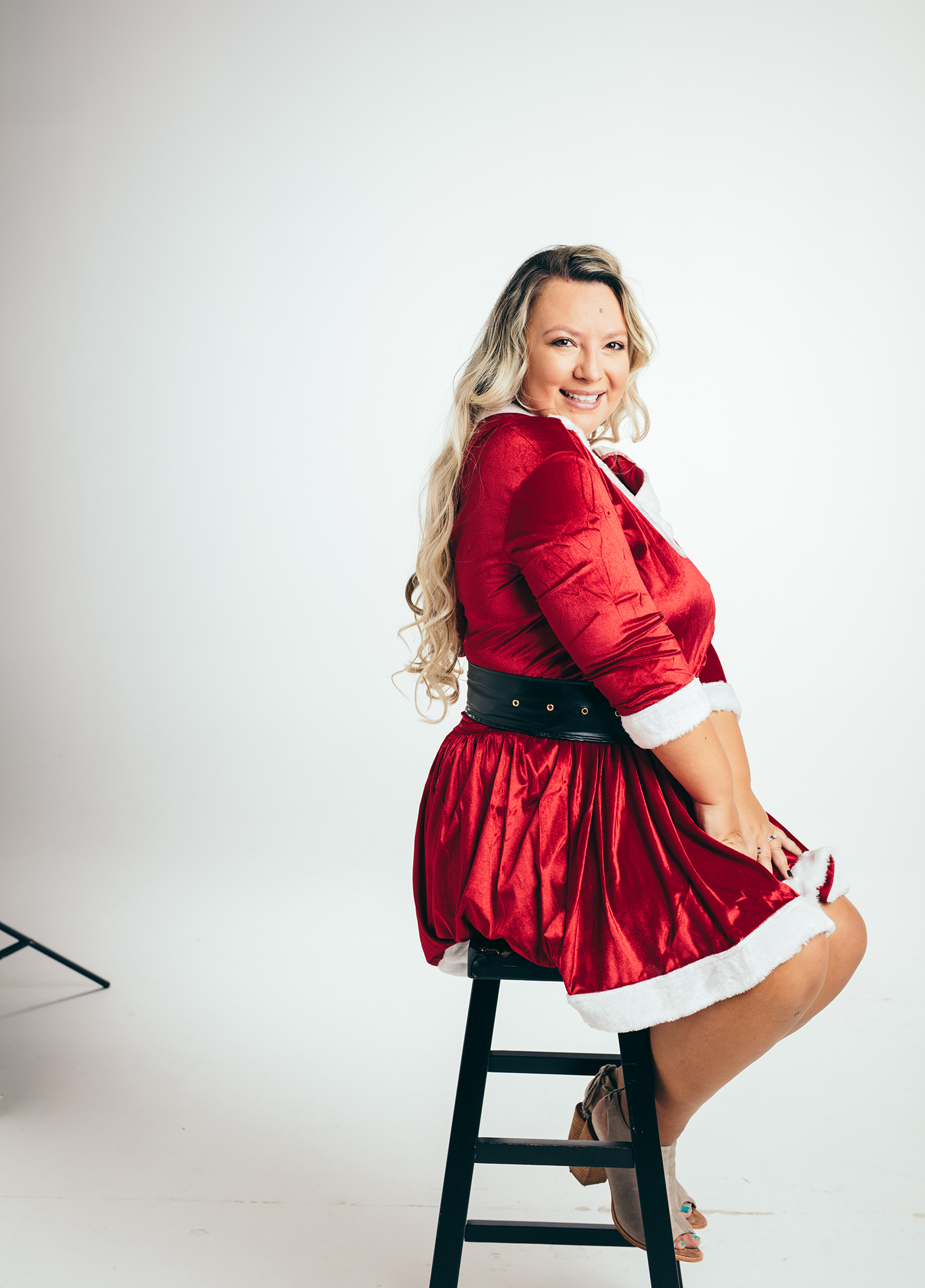 A woman in a santa claus costume sitting on a stool.
