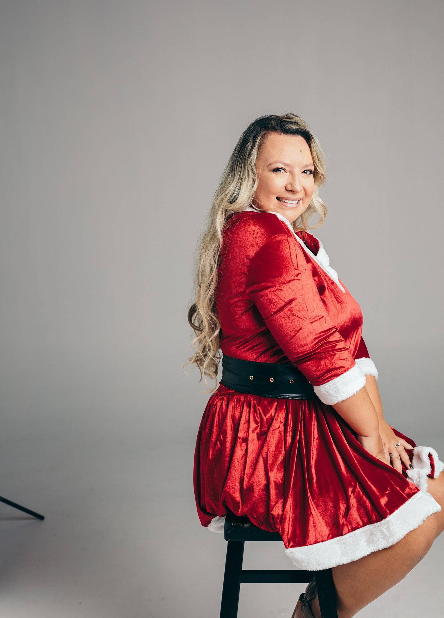 A woman in a santa claus costume sitting on a stool.