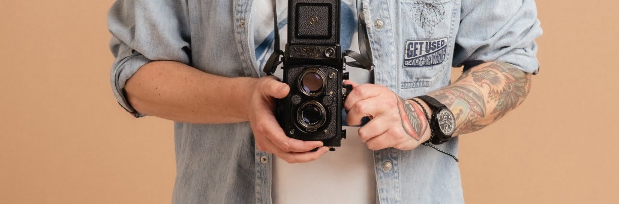 A man with tattoos holding a camera.
