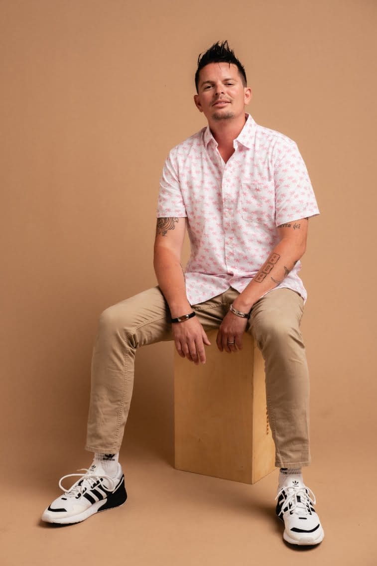 A man in a pink shirt sitting on a wooden box.